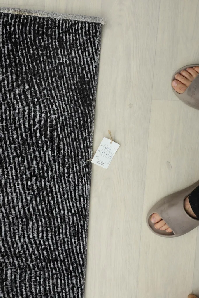 Top-down view of the runner on the floor next to feet, highlighting the rug's tag with product information.