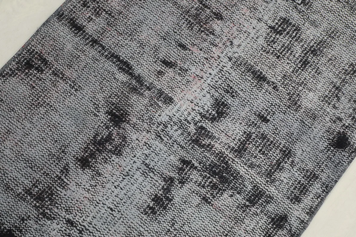 Overhead close-up of the rug's abstract pattern and distressed texture, with shades of charcoal and gray.