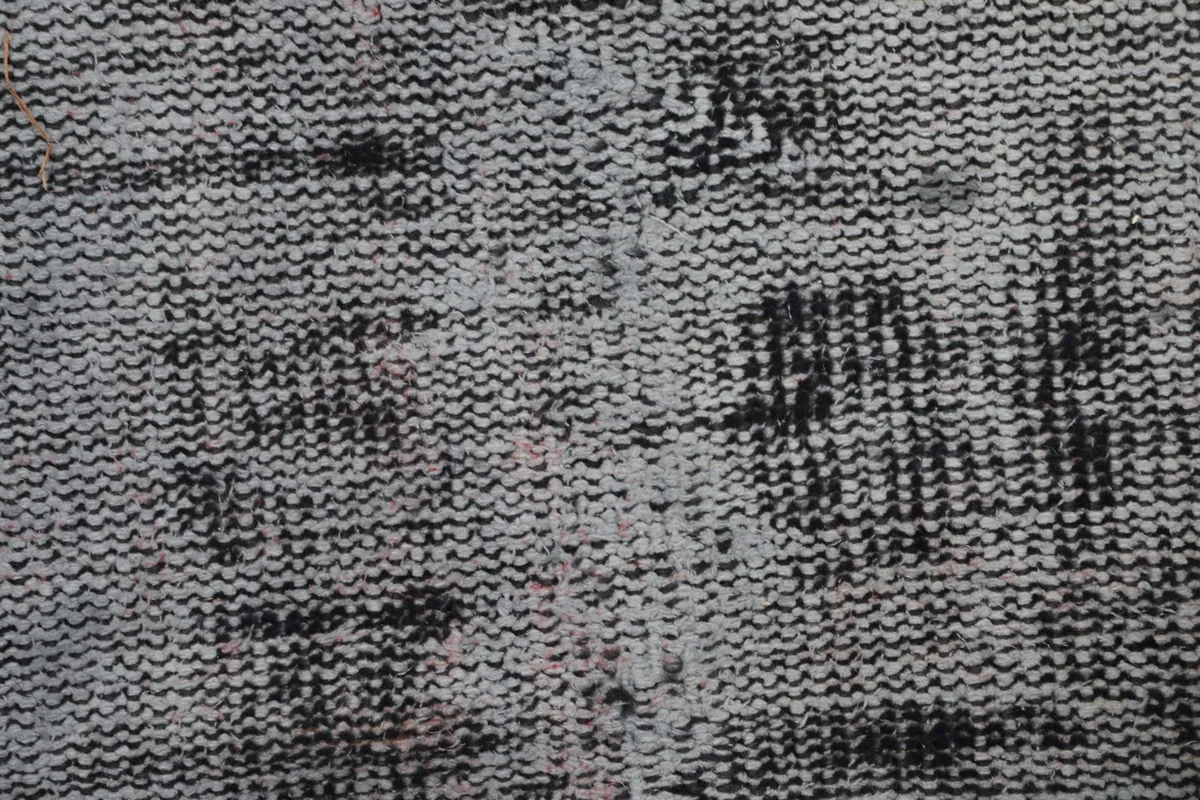 Extreme close-up of the low pile wool surface, revealing the hand-knotted texture and distressed areas.