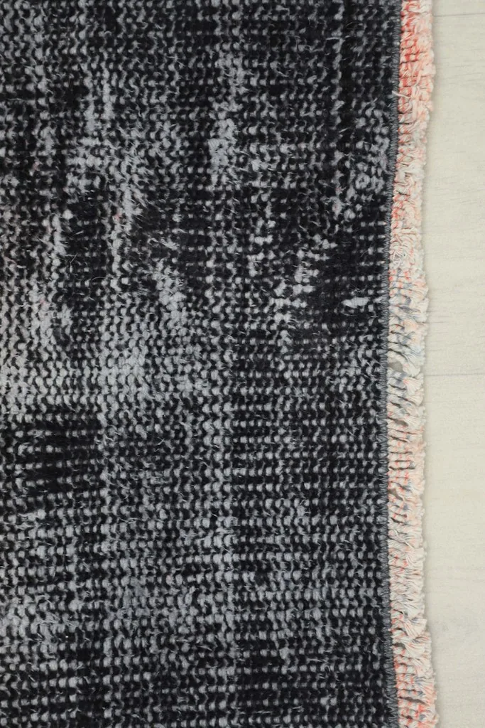 Close-up of the rug's edge, showing the charcoal and gray pile next to the subtle rose-colored fringe.