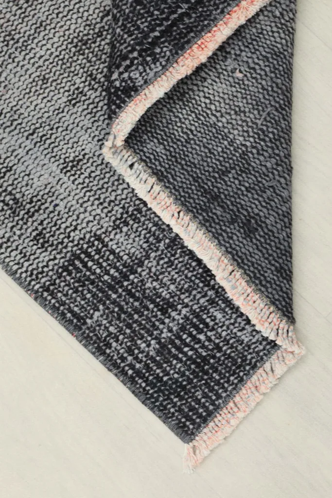 Folded corner of the rug, displaying the thickness of the wool pile and cotton foundation with rose fringe.