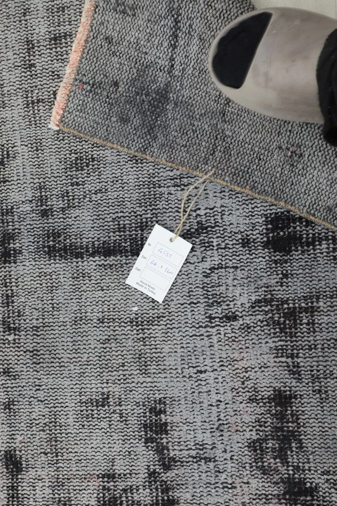 Overhead view of the rug with a tag, showcasing the distressed charcoal and gray pattern and rose fringe.