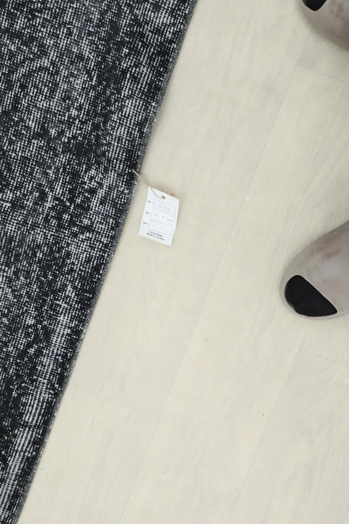 Overhead view of a small tag on the floor next to the charcoal runner, with a person's feet visible.