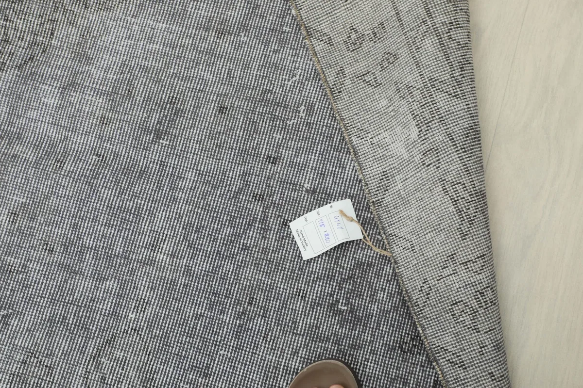 Overhead detail of the rug's label and texture, with a foot for scale