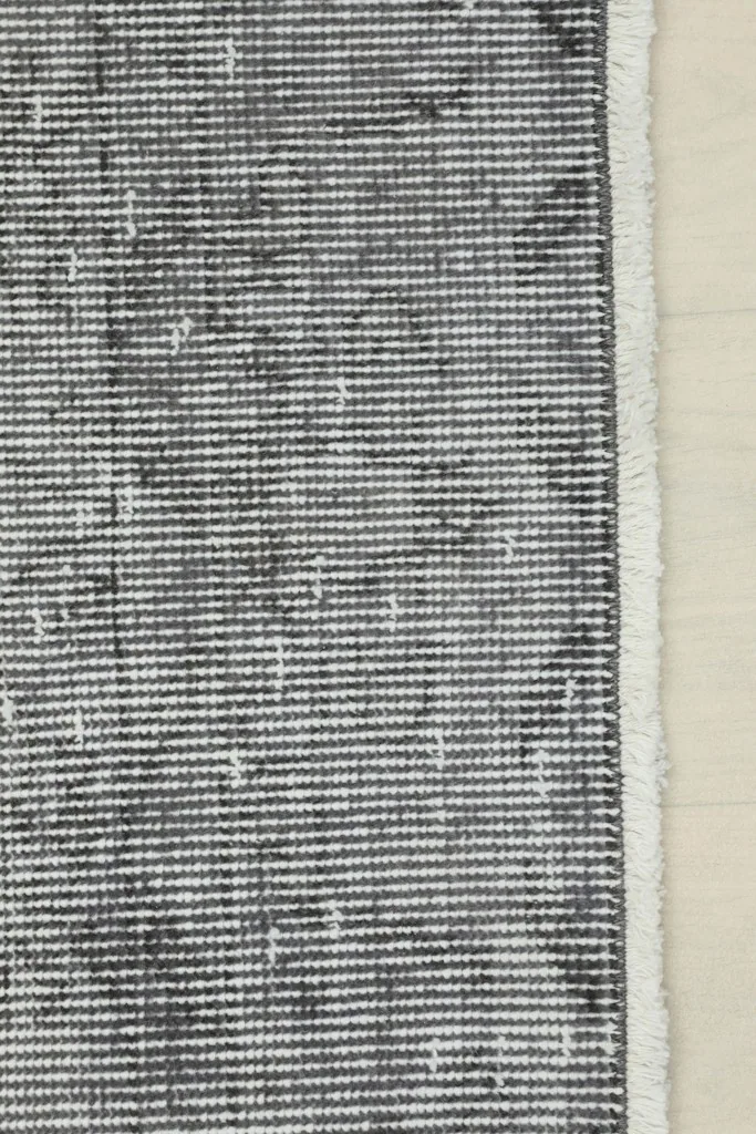 Detail of the rug's edge and fringe, with the distressed charcoal gray pile