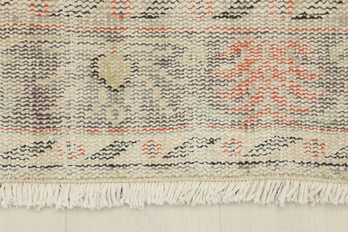 Close-up of the short, natural ivory cotton fringes at the end of the vintage rug.