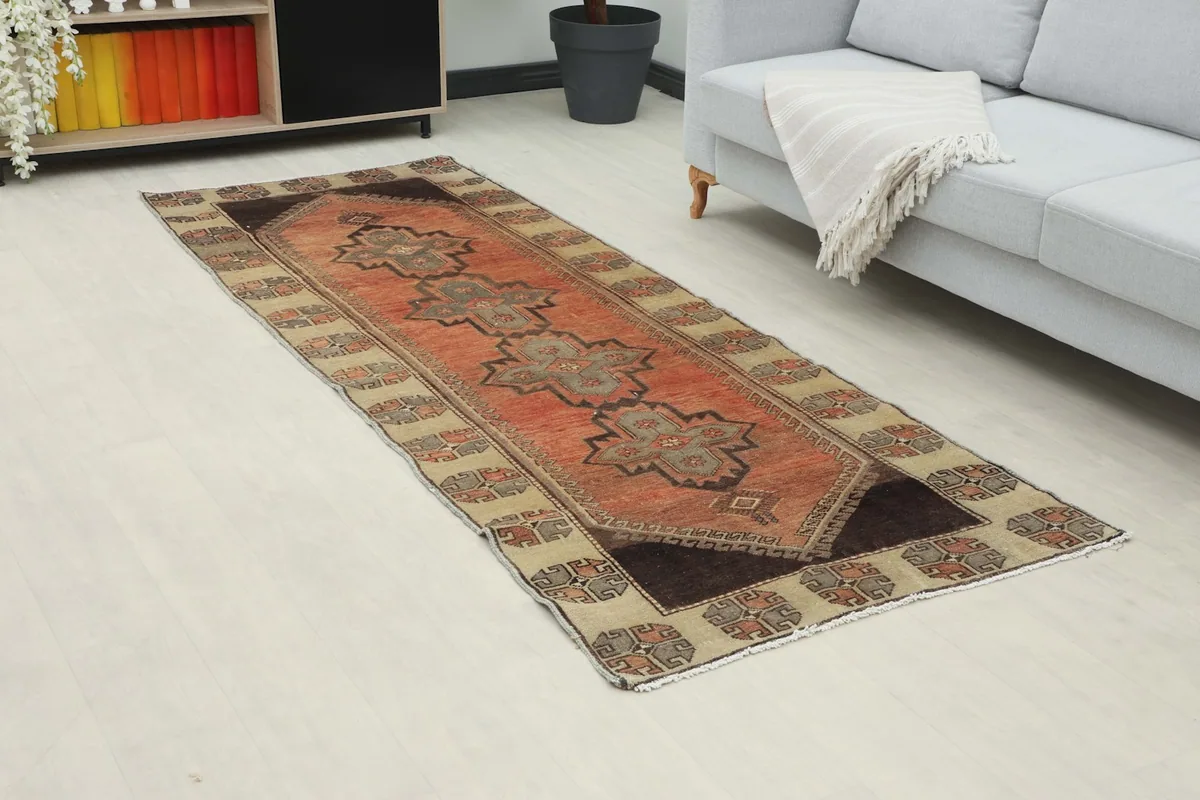 Angled view of the rust runner rug in a room, showing its length and colors next to a sofa.