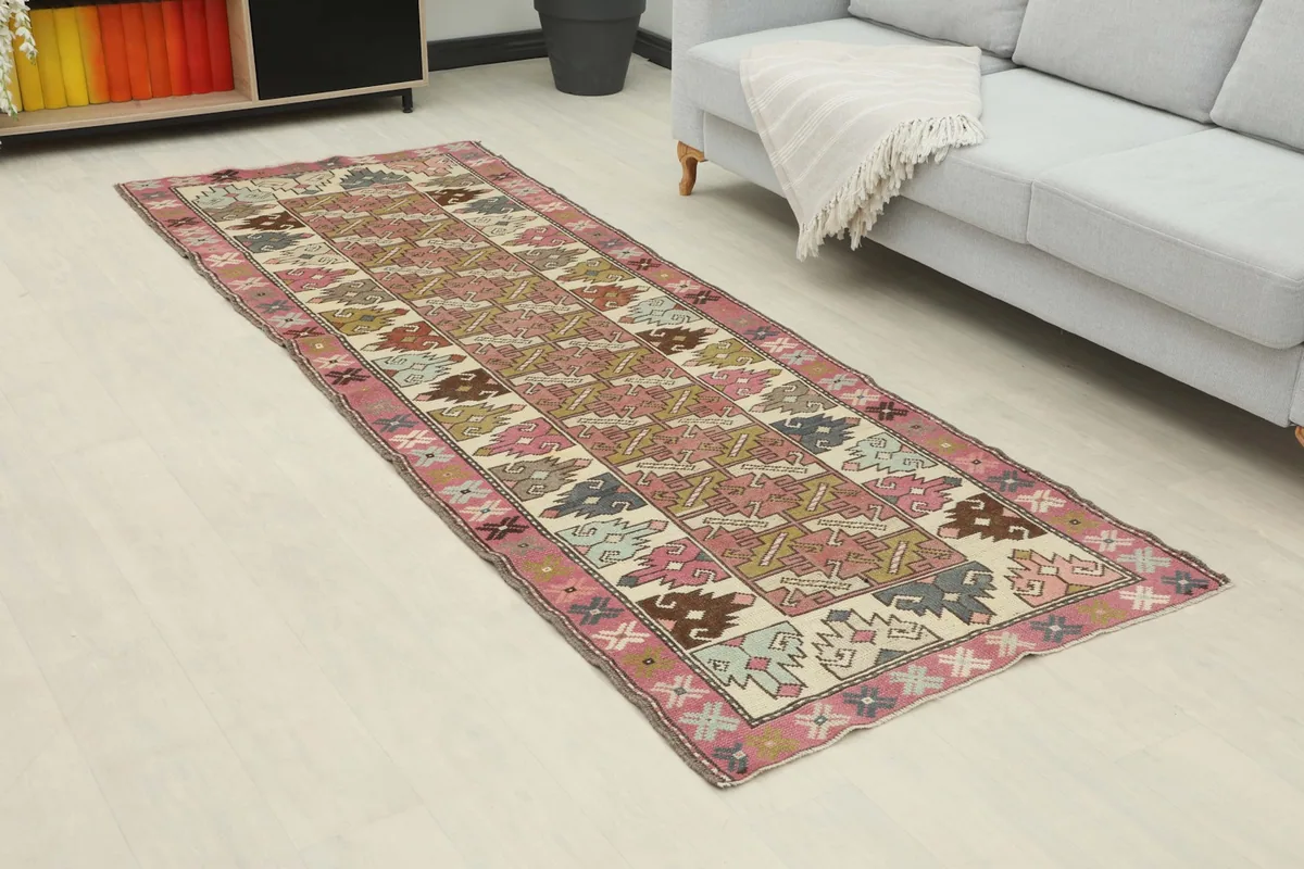 Angle view of the runner rug in a room, highlighting its vibrant rose and ivory geometric design and length.