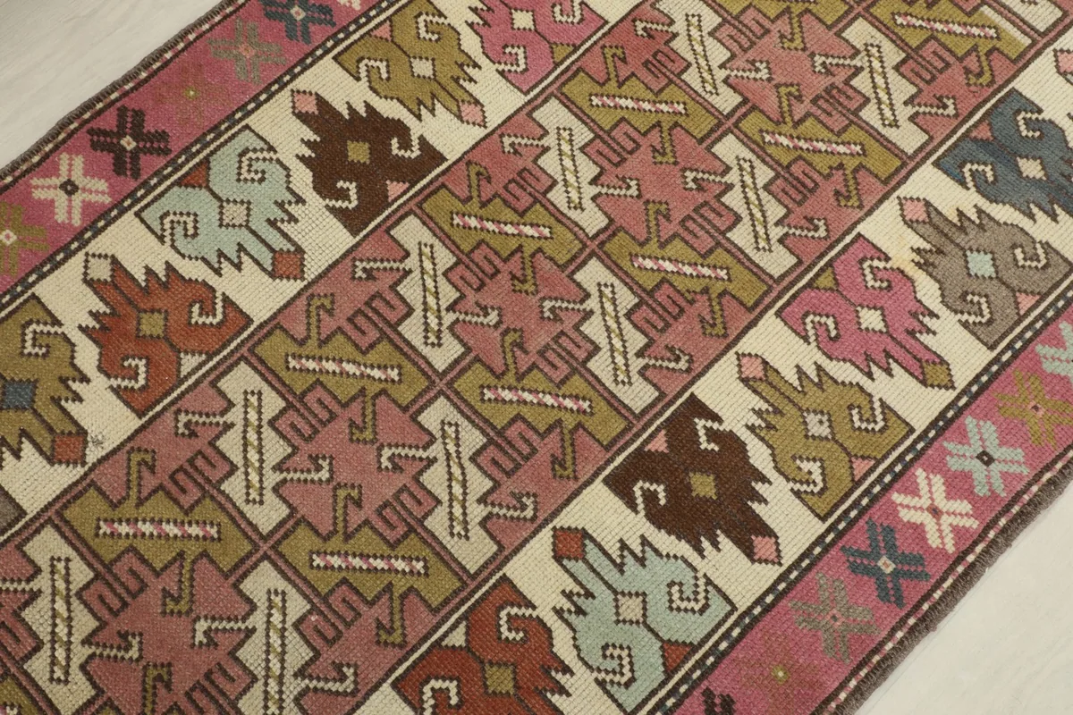 Detailed overhead shot of the rug's central geometric patterns in rose, ivory, olive, and brown tones.