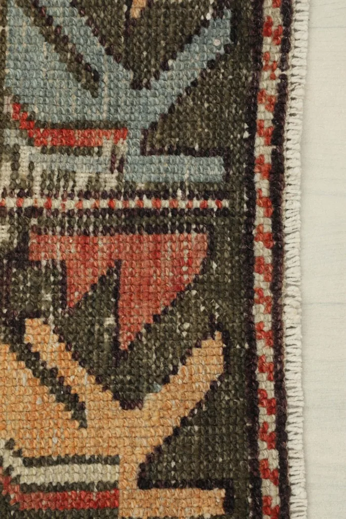 Close-up of the rug's border design featuring tribal motifs in olive, blue, and red with finished edge