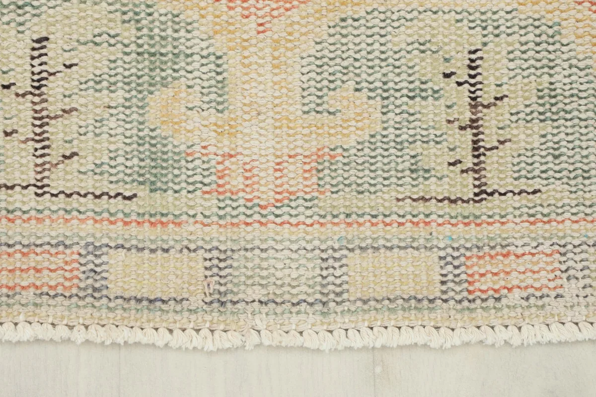 Detail of the rug's border and fringe, showing the beige, gray, and rust colors and aged texture.