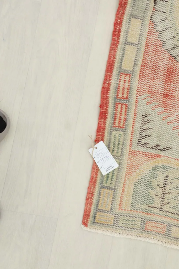 Corner of the rug with a product tag, displaying the overall color scheme and texture of the rust and ivory rug.