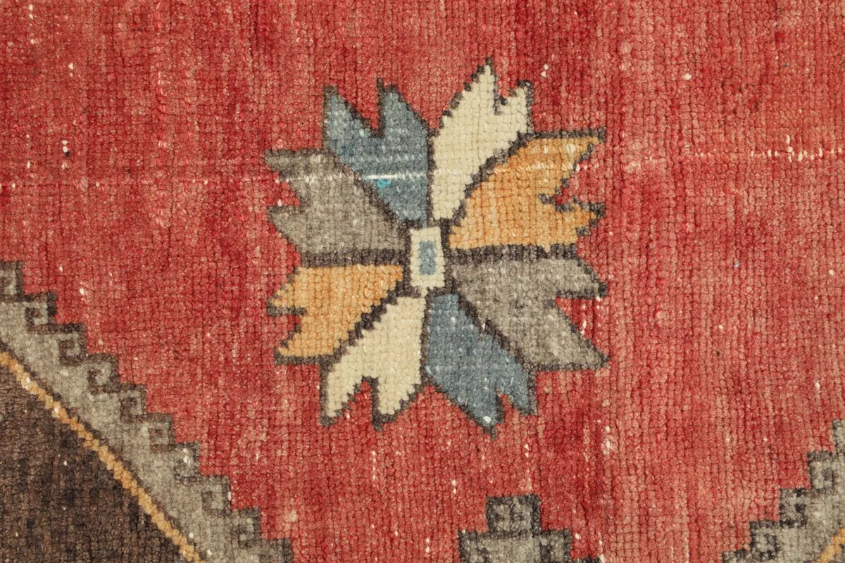 Close-up of a decorative accent motif in blue, yellow, ivory, and gray on the red field.