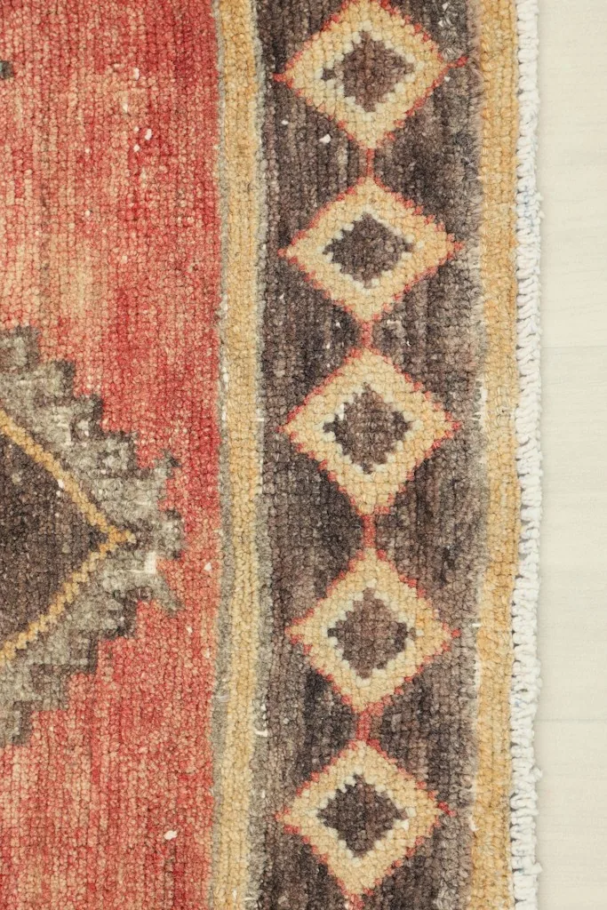 Detailed shot of the rug's side border with diamond patterns in brown and tan.