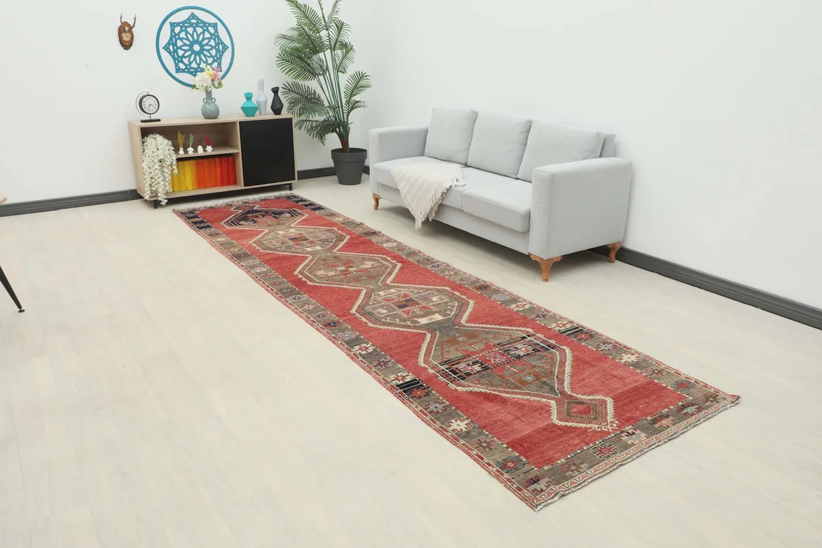 Long shot of the rust and gray runner rug placed in a modern hallway with a light gray sofa and wooden cabinet.