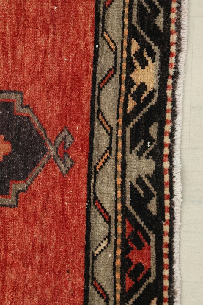 Close-up of the rug's border, featuring gray and black geometric motifs and short fringe
