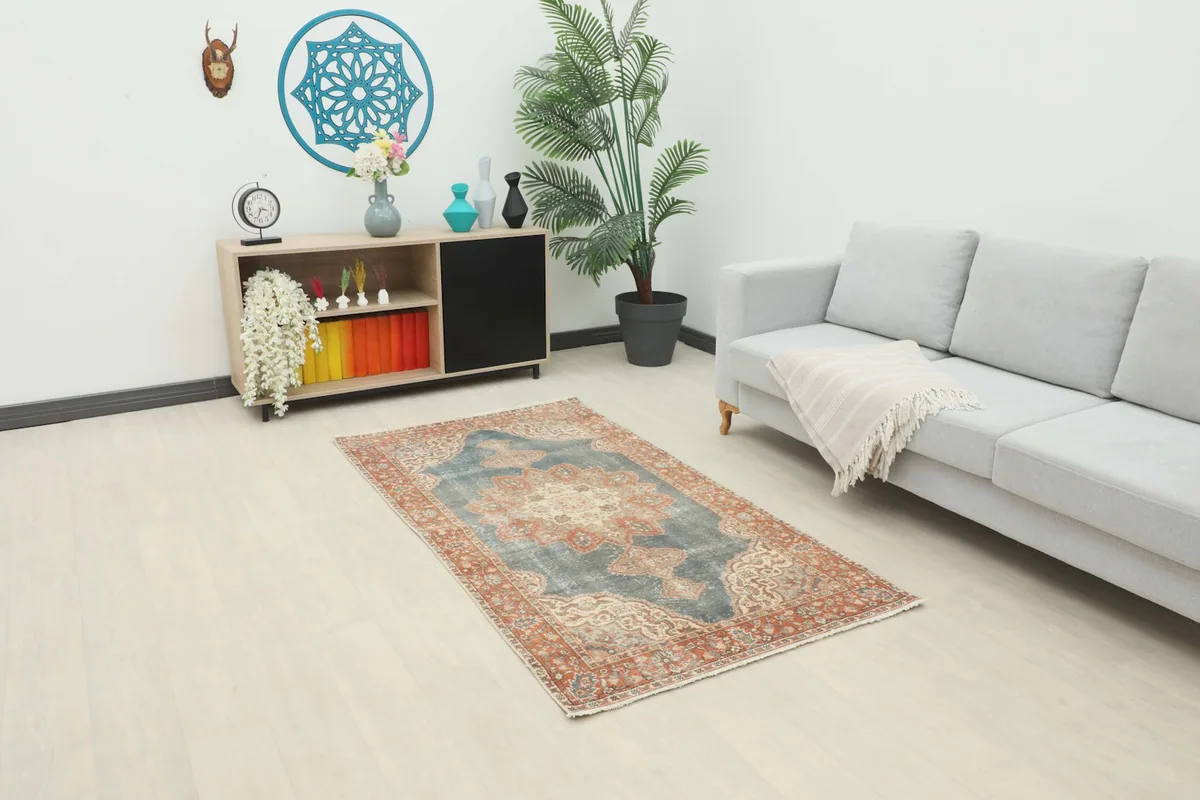 Vintage blue and rust rug placed in a living room setting next to a gray sofa and wooden cabinet