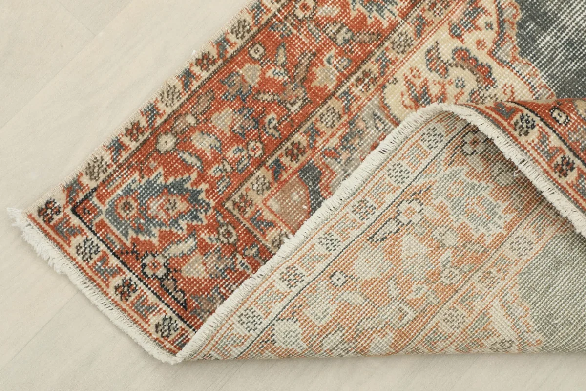 Corner of the rug folded back, revealing the cotton foundation and the reverse side of the hand-knotted construction