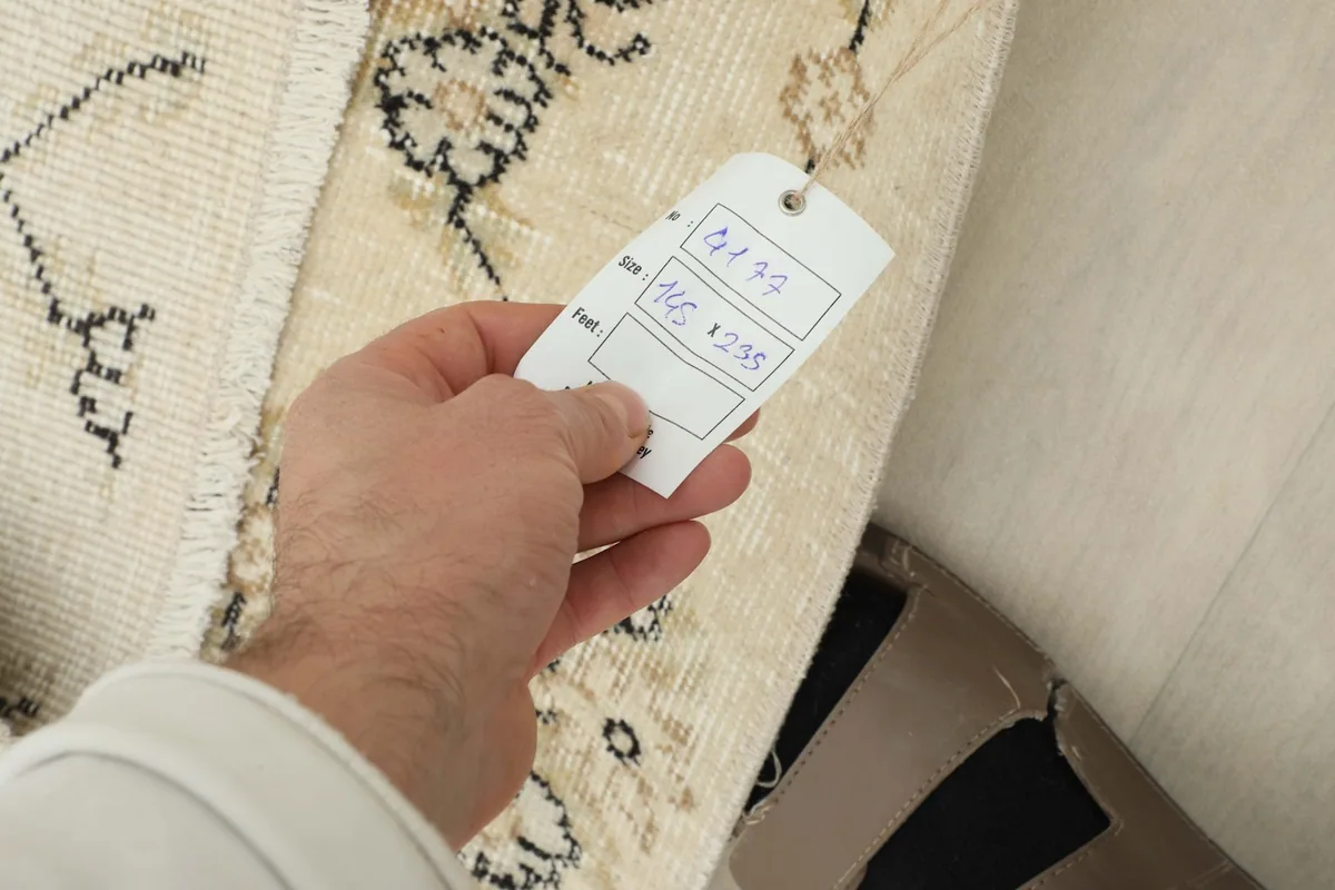 Hand holding a size tag over the rug, confirming its dimensions of 145 x 235 cm