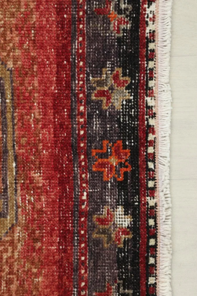Detail of the rug's border, showcasing the red, black, and orange patterns near the fringe