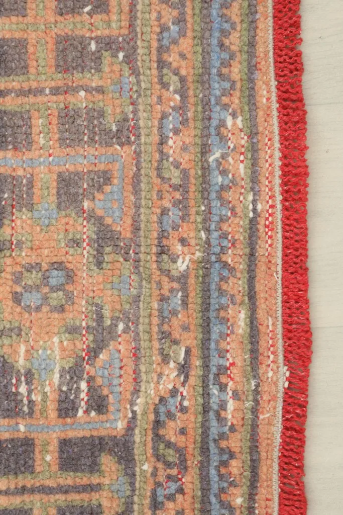 Detail of the side border and red-wrapped edge, showing wear consistent with a vintage rug