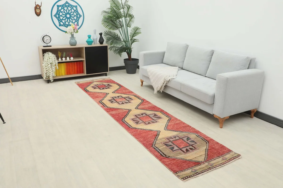 Vintage red and beige runner rug laid out in a modern living space with a gray sofa and wooden furniture.