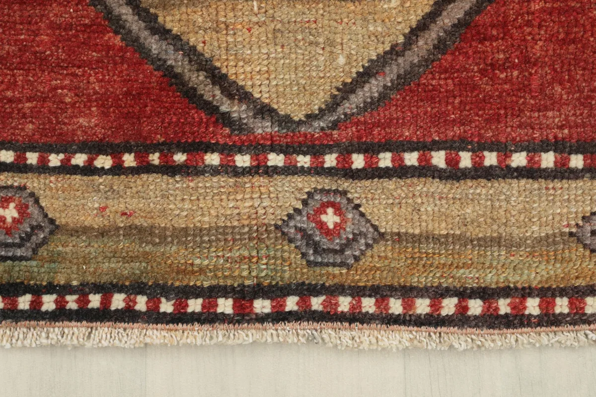 Close-up of the rug's border, featuring intricate patterns in beige, brown, red, and gray.