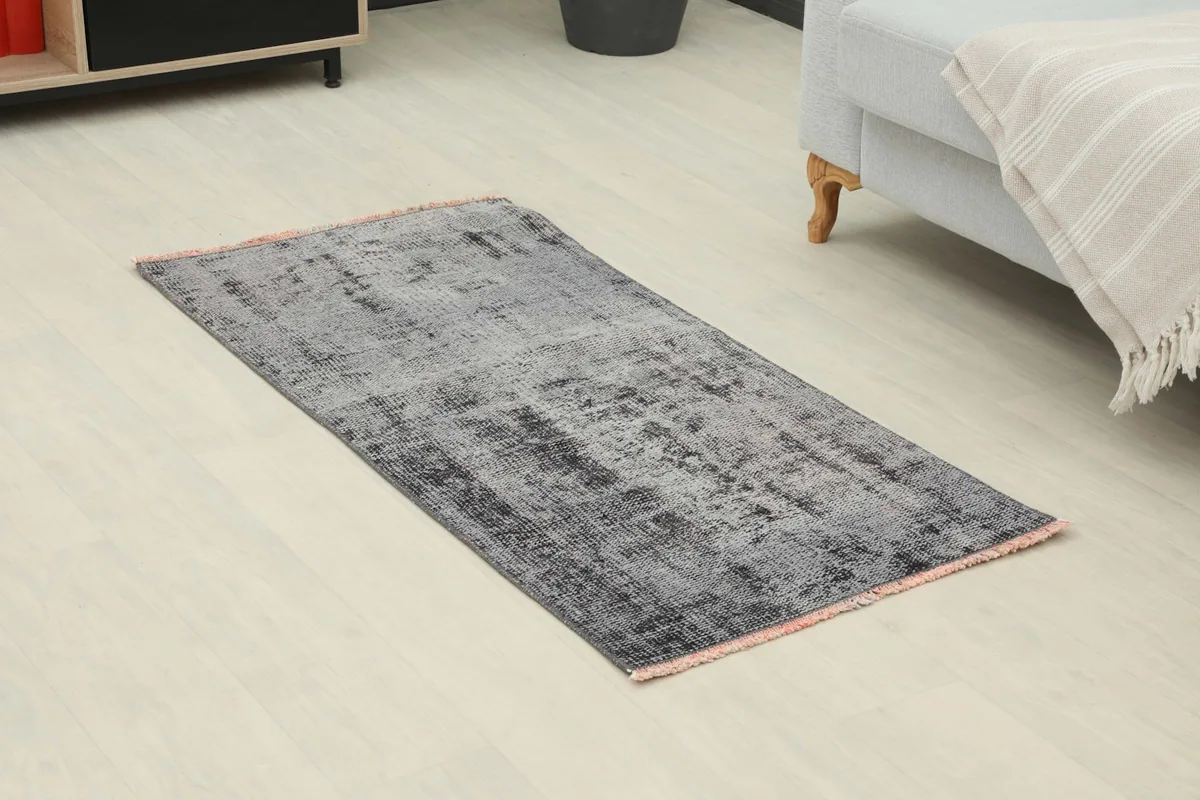 Angle view of the distressed gray and charcoal rug on a light floor next to a sofa