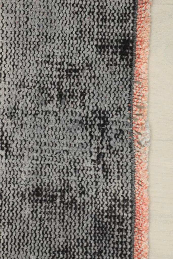 Detail of the rug's edge, showing the subtle pink fringe and the charcoal and gray pile