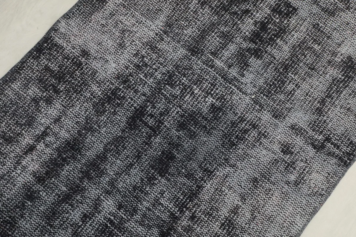 Close-up detail of the distressed charcoal and gray wool pile, revealing the underlying texture