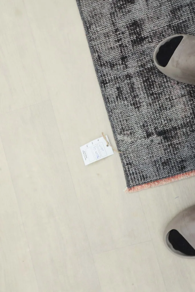Overhead view showing the rug with a tag and a pair of feet, indicating its scale