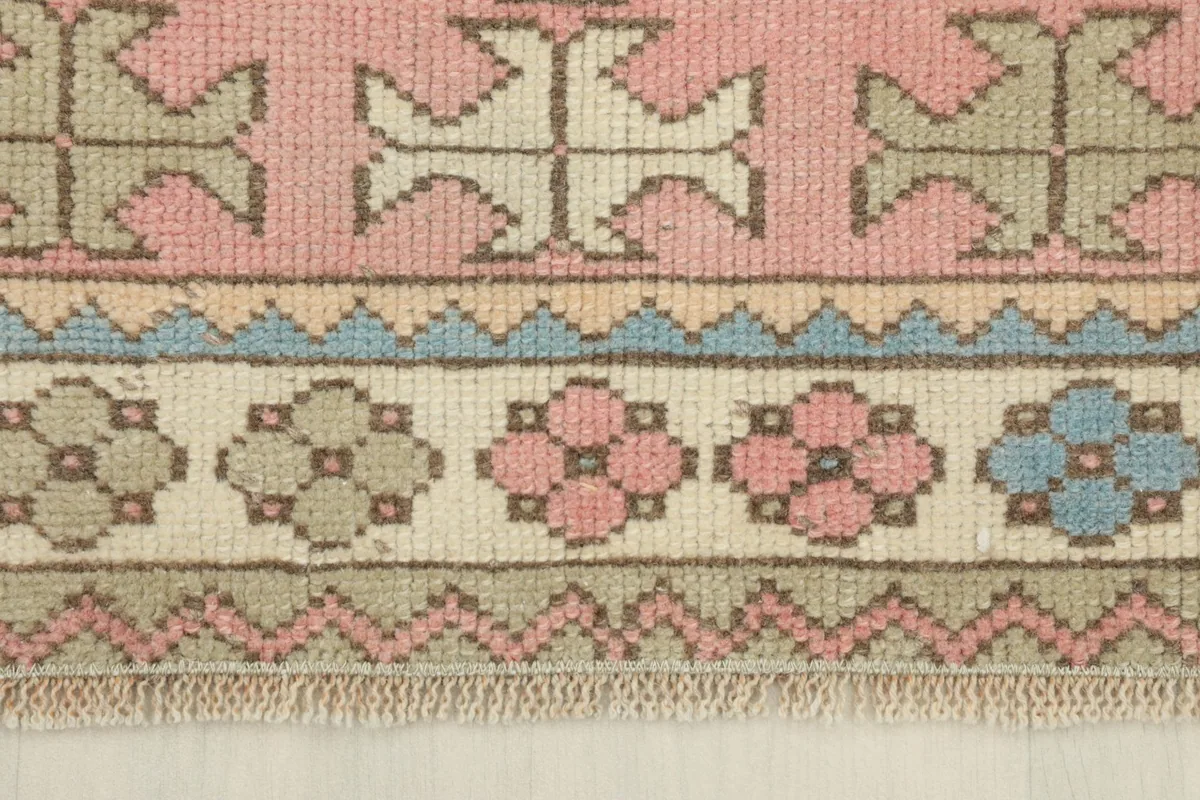 Detailed view of the rug's border, showing small floral-like patterns in pink, blue, and gray on a beige band