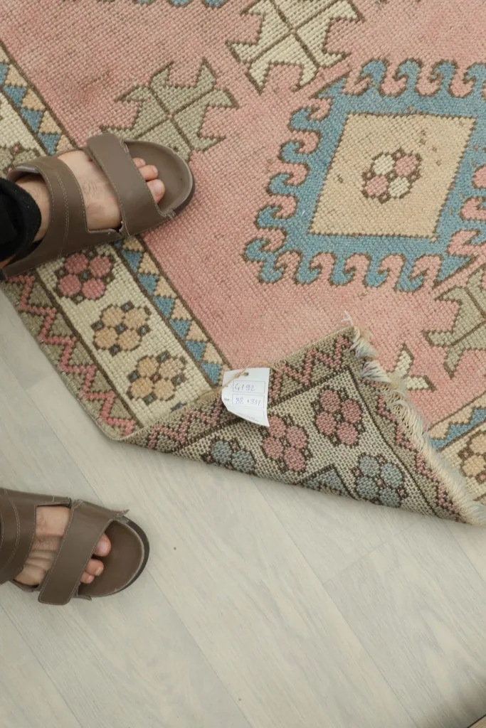 Close-up of the rug's reverse side and fringe, with feet in sandals for scale, showing hand-knotted construction