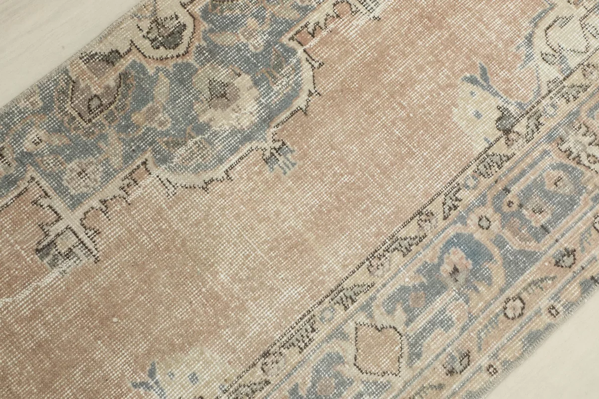 Detailed view of the rug's distressed central area with tan, blue, and cream tones