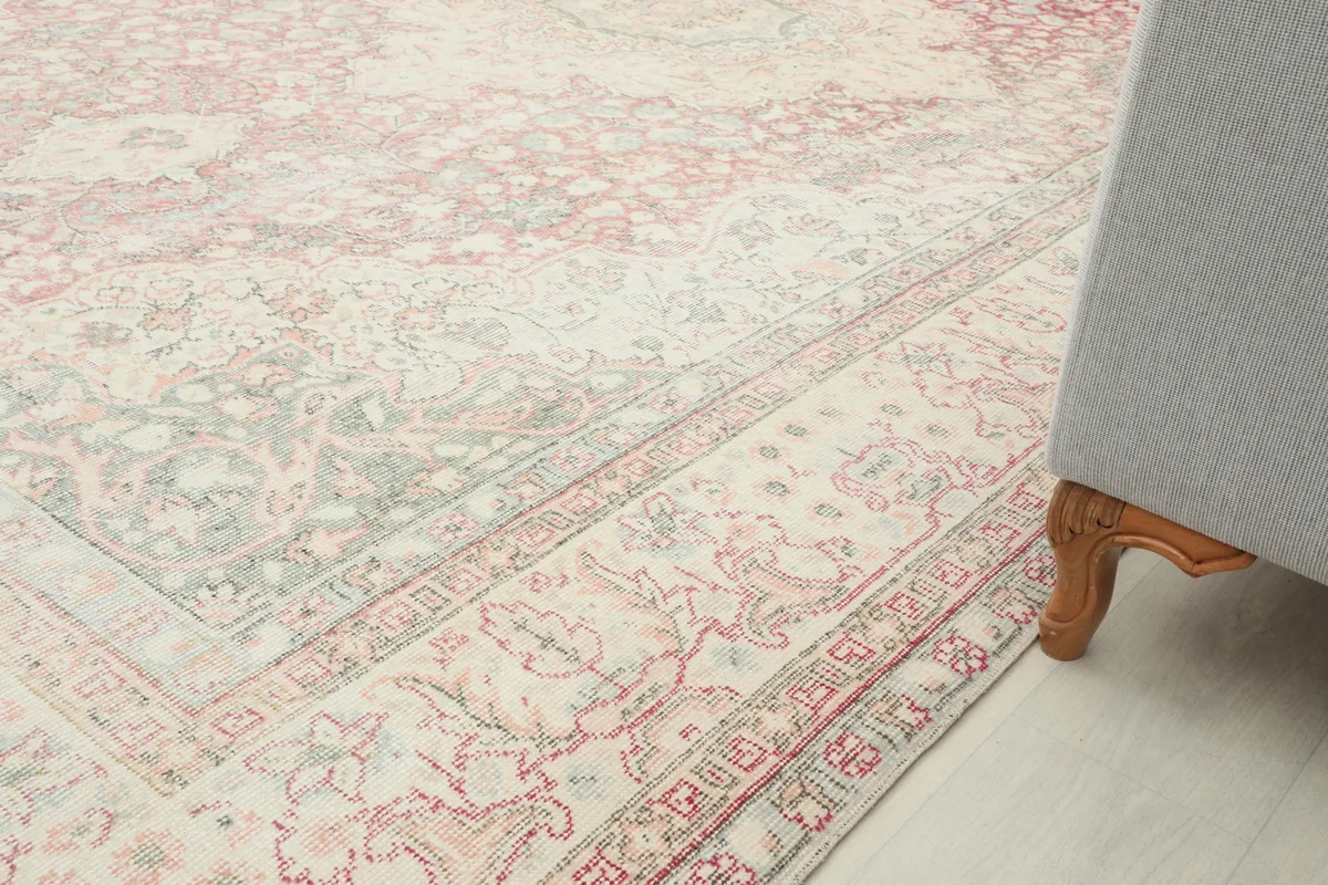 Close-up of the border design of the Rose Ivory Medallion Anatolian Rug next to a sofa leg, showing subtle patterns.