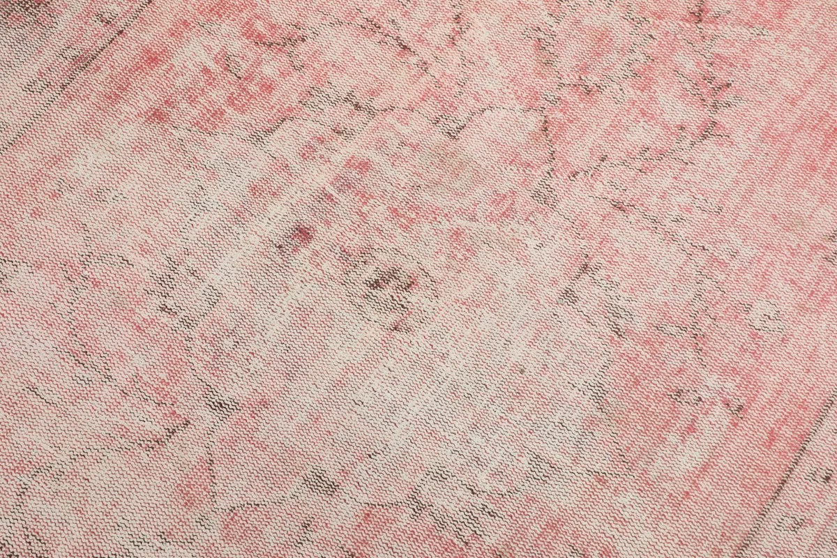 Detailed view of the rug's low pile, showing the faded rose and cream wool fibers.