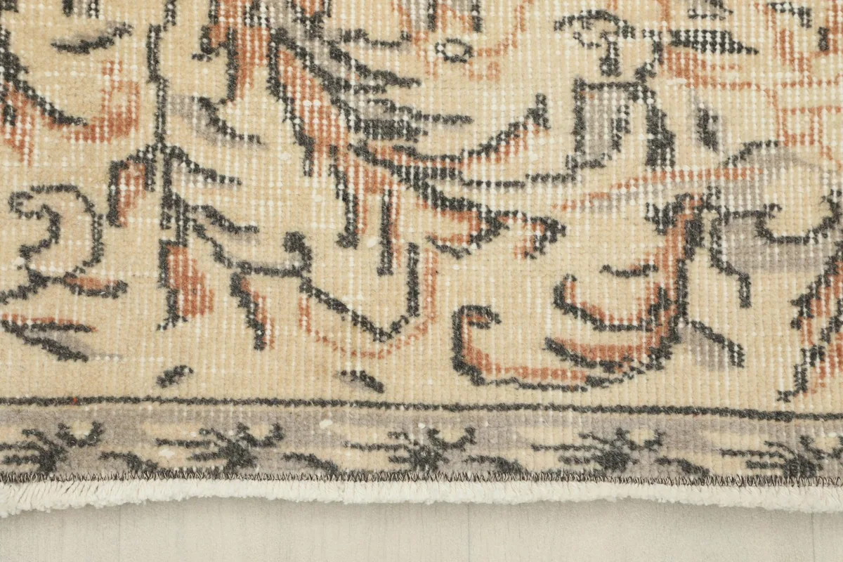 Detail of the rug's outer border and short fringe, with beige and gray tones.