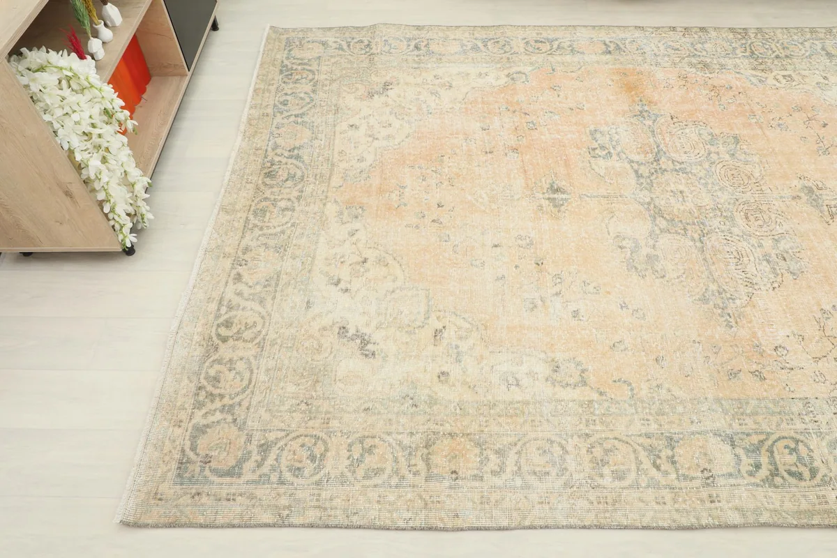 Corner view of the rug, highlighting the worn patina and the blend of orange, blue, and cream colors