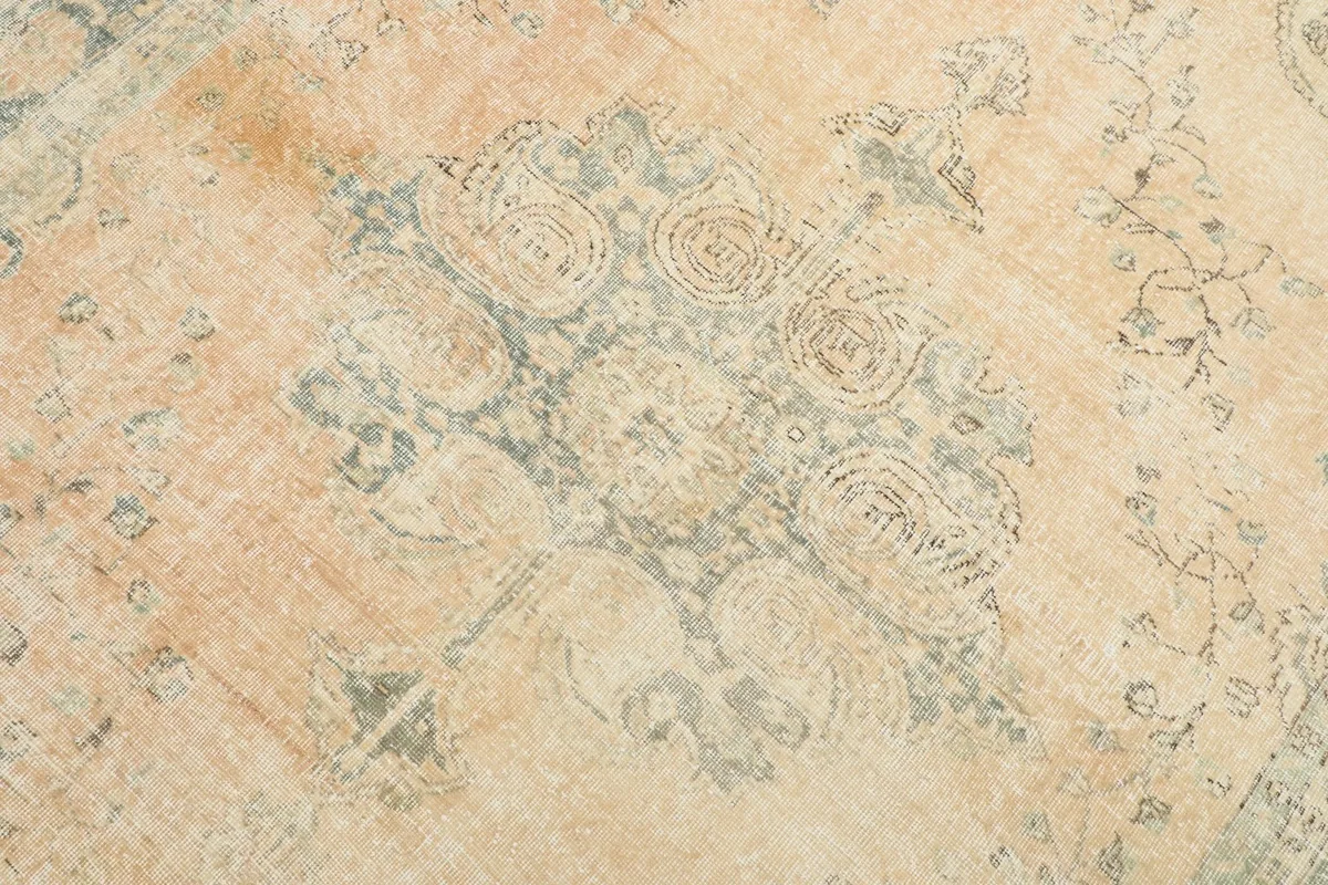 Detail of the central medallion design, showing the faded blue and cream motifs on the orange background