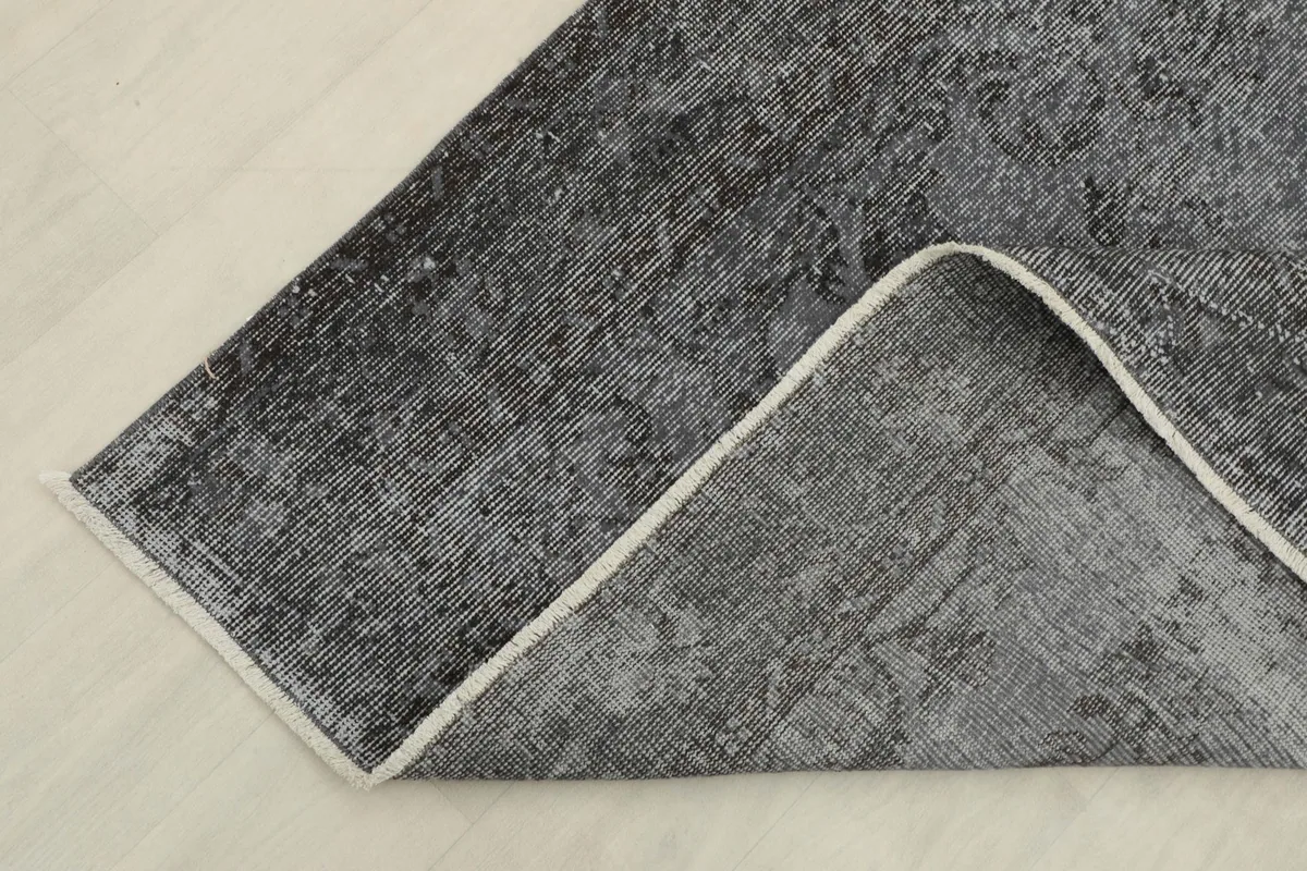 Corner of the rug folded back, showing the cotton foundation and the reverse side of the hand-knotted wool.