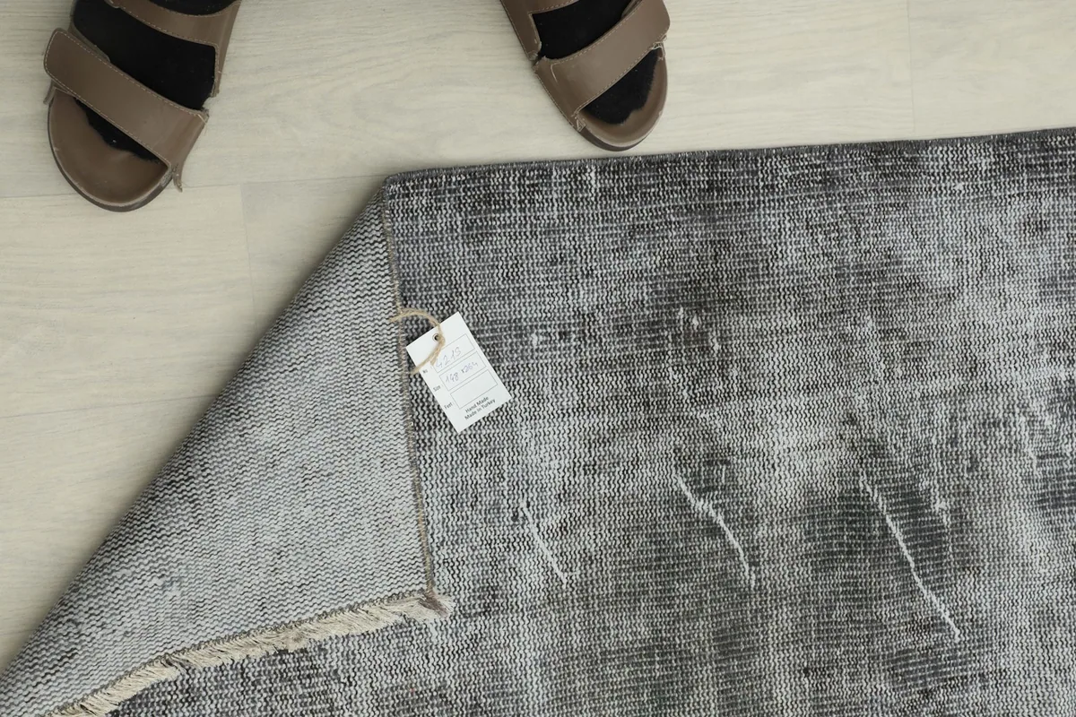 Overhead view showing the rug's tag and a pair of feet for scale, emphasizing its vintage origin