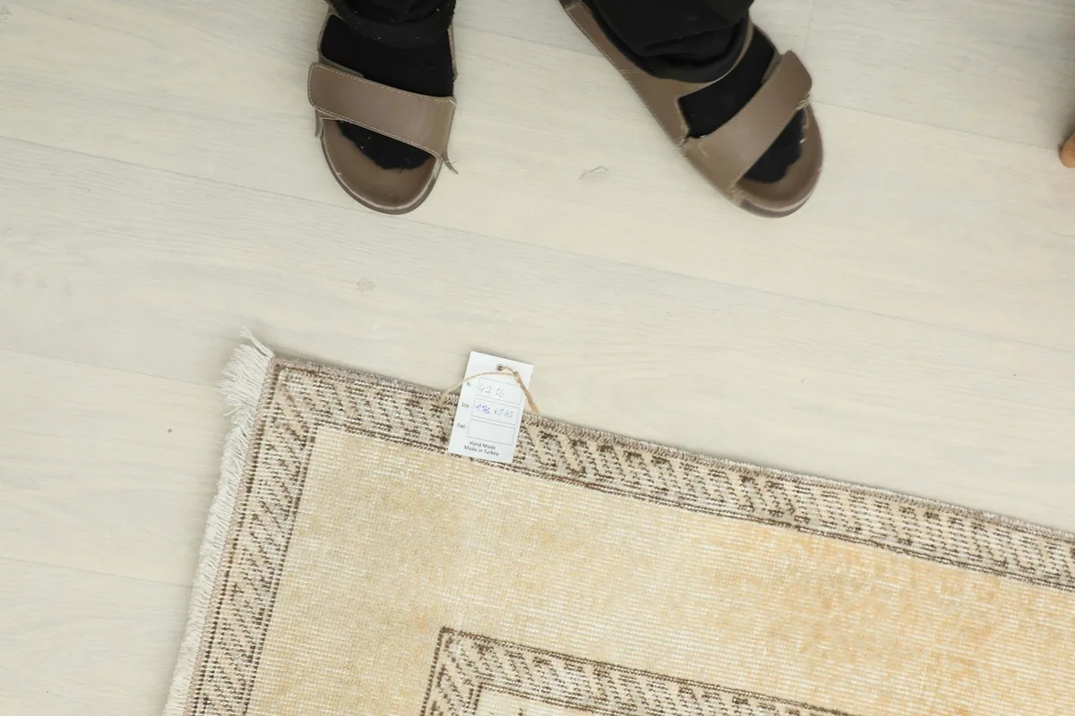 Overhead view of a person's feet near the rug, showing its scale and a product tag