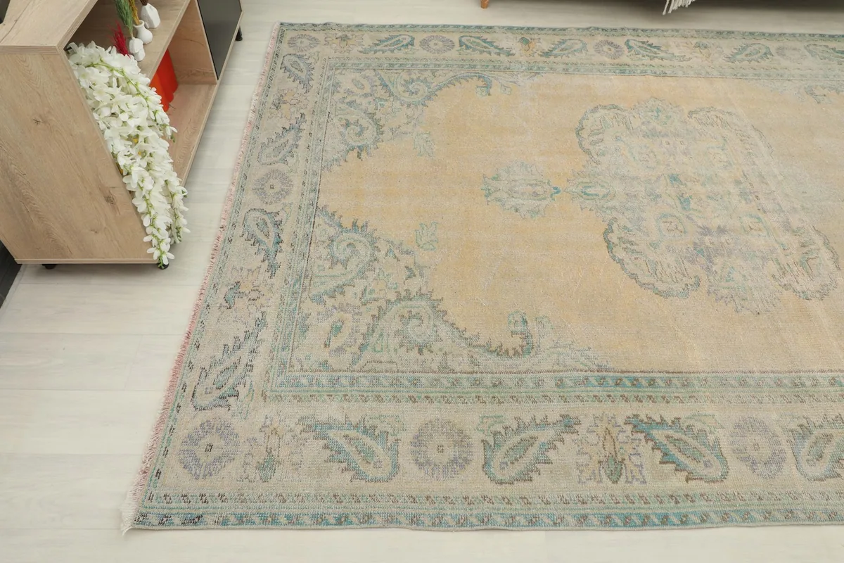 Corner view of the vintage rug, showing the beige field and green motifs with subtle wear