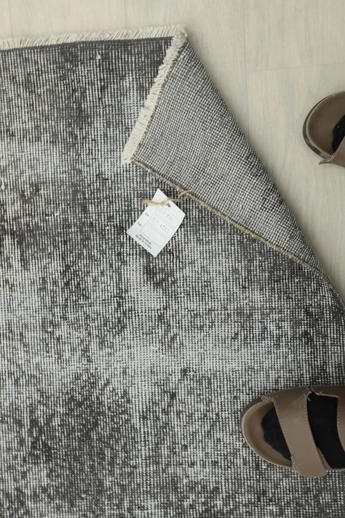 Overhead view of the rug with a tag and sandals, indicating its size and vintage authenticity.