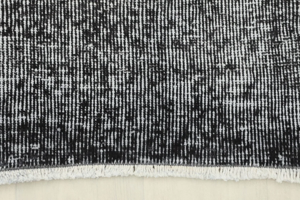 Detail of the short, subtle fringes and the end of the charcoal vintage rug.