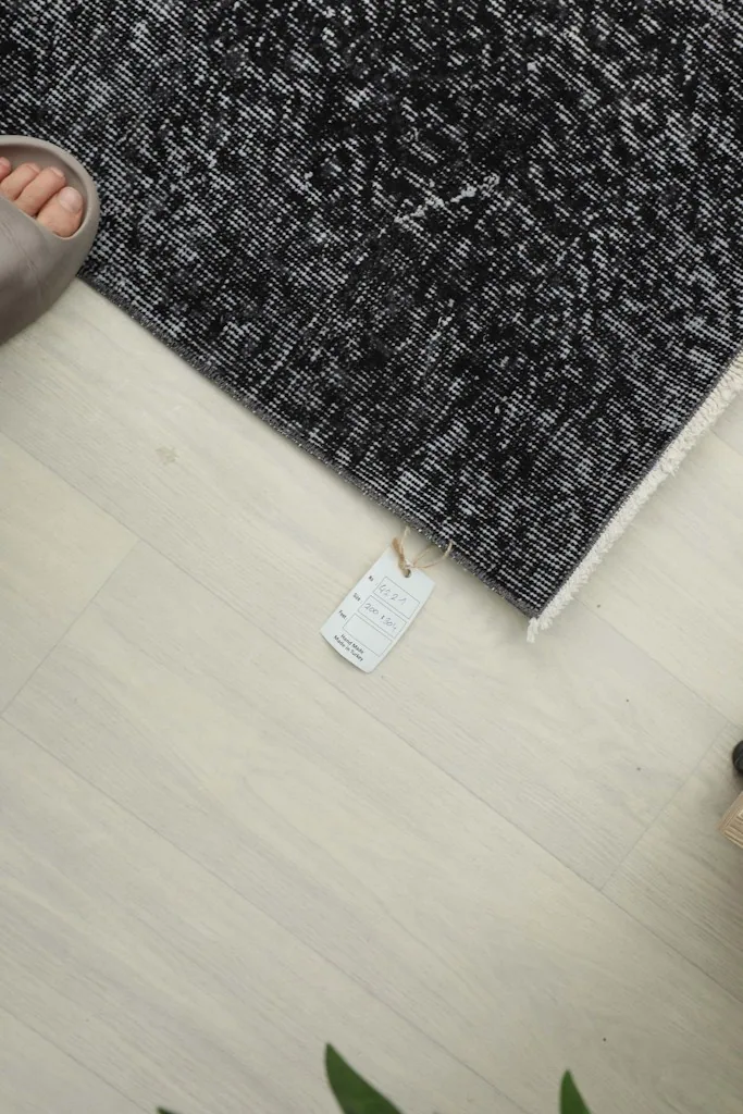 Top-down view of a corner of the rug with the product tag, showing scale next to a foot.