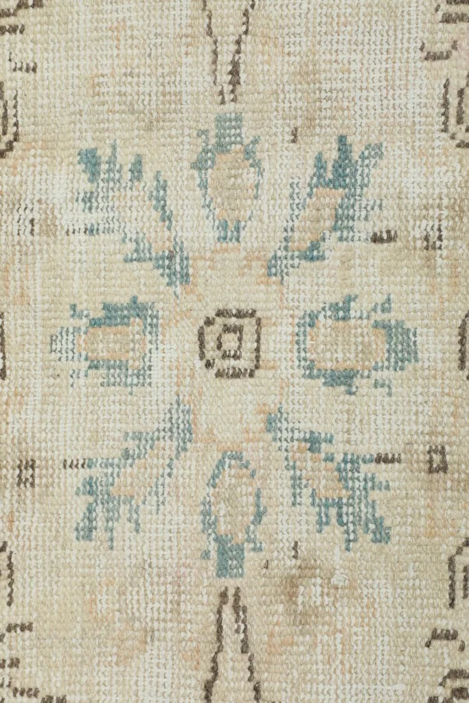 Extreme close-up of the wool pile and hand-knotted texture, revealing beige, blue, and brown threads.