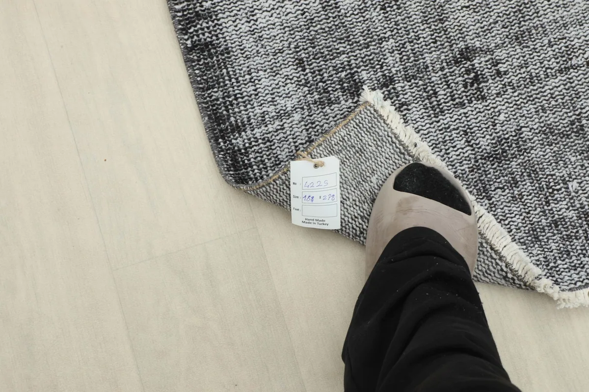 Close-up of the rug corner with a size tag, next to a foot for scale