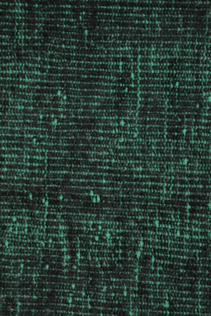 Close-up of the low pile, showcasing the texture and varying shades of green and black from distress.