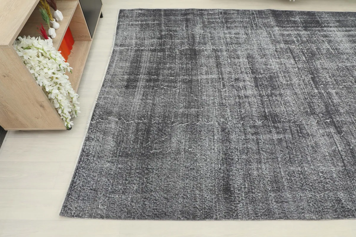 Close-up angled view of the distressed vintage rug, showing the faded patterns and charcoal tones.